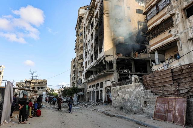 People walk past a residential building that was hit by an Israeli strike the previous day in the Rimal neighbourhood of Gaza City on May 16, 2026. Israel said on May 15 that it carried out a strike in Gaza targeting Ezzedine Al-Haddad, who described it as chief of the armed wing of Palestinian movement Hamas. Since Hamas's October 7, 2023 attack on Israel, the Israeli military and intelligence services have waged an extensive campaign targeting the group's senior political leaders and militant commanders in Gaza and across the region. (Photo by Omar AL-QATTAA / AFP)