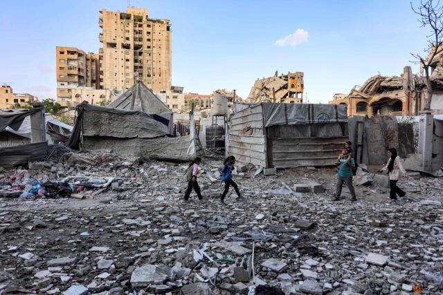 People walk outside a residential building that was hit by an Israeli strike the previous day in the Rimal neighbourhood of Gaza City on May 16, 2026. Israel said on May 15 that it carried out a strike in Gaza targeting Ezzedine Al-Haddad, who described it as chief of the armed wing of Palestinian movement Hamas. Since Hamas's October 7, 2023 attack on Israel, the Israeli military and intelligence services have waged an extensive campaign targeting the group's senior political leaders and militant commanders in Gaza and across the region. (Photo by Omar AL-QATTAA / AFP)