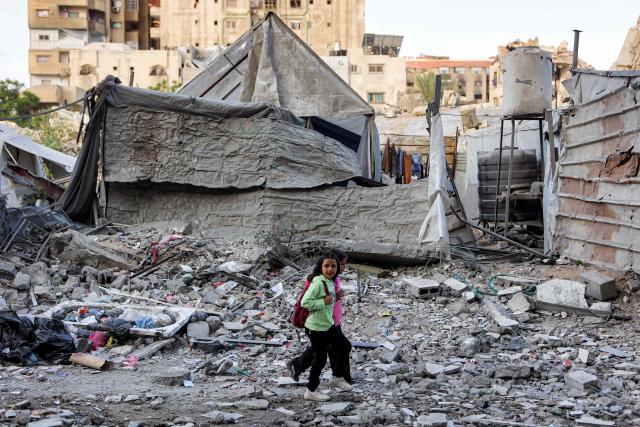Children walk outside a residential building that was hit by an Israeli strike the previous day in the Rimal neighbourhood of Gaza City on May 16, 2026. Israel said on May 15 that it carried out a strike in Gaza targeting Ezzedine Al-Haddad, who described it as chief of the armed wing of Palestinian movement Hamas. Since Hamas's October 7, 2023 attack on Israel, the Israeli military and intelligence services have waged an extensive campaign targeting the group's senior political leaders and militant commanders in Gaza and across the region. (Photo by Omar AL-QATTAA / AFP)