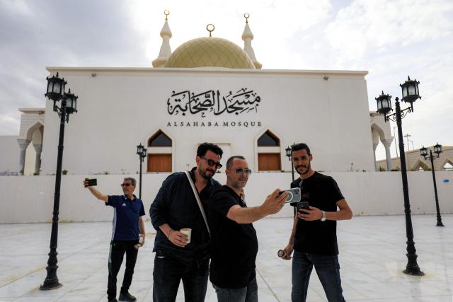 People pose for a group "selfie" picture together on a phone outside the Sahaba in Mosque Libya's eastern city of Derna on May 15, 2026, following reconstruction and reurbanisation efforts over two years after after extreme rainfall from the hurricane-strength Storm Daniel caused two dams to burst and cause flooding, killing thousands and razing entire neighbourhoods in the city. (Photo by Abdullah DOMA / AFP)