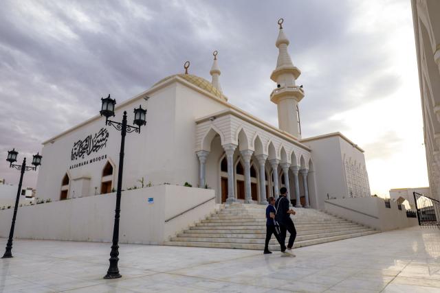 People walk outside the Sahaba Mosque in Libya's eastern city of Derna on May 15, 2026, following reconstruction and reurbanisation efforts over two years after after extreme rainfall from the hurricane-strength Storm Daniel caused two dams to burst and cause flooding, killing thousands and razing entire neighbourhoods in the city. (Photo by Abdullah DOMA / AFP)