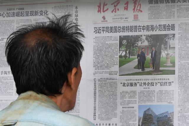 A man reads a newspaper with an article about the visit of US President Donald Trump to Zhongnanhai Garden, hosted by China’s President Xi Jinping, at a newspaper display board in Beijing on May 16, 2026. (Photo by GREG BAKER / AFP)