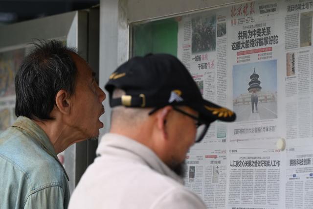 Two men read newspapers, including one with an article about meetings between China’s President Xi Jinping and US President Donald Trump, with a photo of them visiting the Temple of Heaven, at a newspaper display board in Beijing on May 16, 2026. (Photo by GREG BAKER / AFP)
