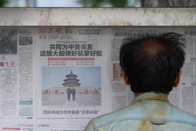 A man reads a newspaper with an article about meetings between China’s President Xi Jinping and US President Donald Trump, with a photo of them visiting the Temple of Heaven, at a newspaper display board in Beijing on May 16, 2026. (Photo by GREG BAKER / AFP)