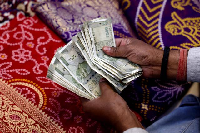 An employee counts Indian rupee currency notes at a shop in Varanasi on May 16, 2026. (Photo by Niharika KULKARNI / AFP)