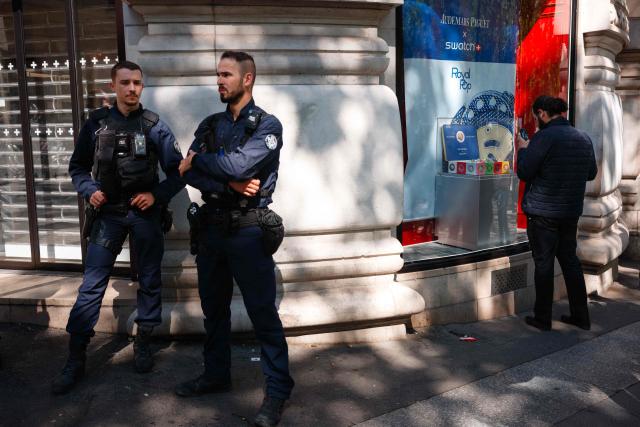 Police officers stand guard outside of a closed shop of Swiss watch company Swatch amid a promotional campaign for their Royal Pop watches in partnership with luxury Swiss watch maker Audemars Piguet in Paris on May 16, 2026. The collaboration between the two Swiss watch brands was highly anticipated by fans with some clients waiting for days ahead of the release, sometimes creating tension near shops in France. (Photo by Dimitar DILKOFF / AFP)