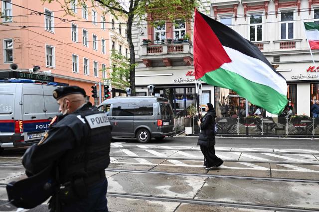 A woman waves a huge Palestinian flag as she walks past police during a pro-Palestinian demonstration under the motto 'Song Protest Vienna 2026 - No Stage for Genocide' against Israel's participation in the Eurovision Song Contest (ESC), in Vienna, Austria, on May 16, 2026. (Photo by Joe Klamar / AFP)
