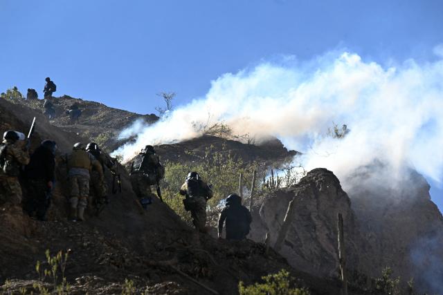 Riot police officers advance along a hillside amid tear gas during clashes with rural protesters in Lipari, La Paz department, Bolivia, on May 16, 2026. Bolivia's government reached an agreement on May 15 with thousands of miners who clashed with police in a protest that paralysed downtown La Paz. However, other sectors continue to block access routes to the city, home to the executive branch and Congress. (Photo by AIZAR RALDES / AFP)