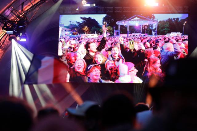 Spectators gather at the fan area as a flag with the national colors of France waves in front of the giant screen prior to the final of the Eurovision Song Contest 2026 (ESC) outside the City Hall in Vienna, Austria on May 16, 2026. (Photo by Alex HALADA / AFP)