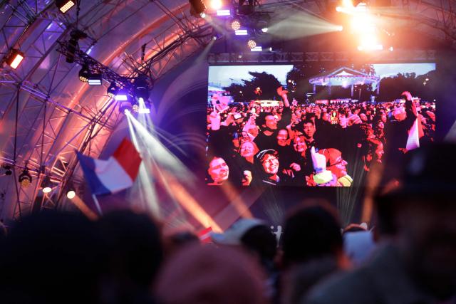 Spectators gather at the fan area as a flag with the national colors of France waves in front of the giant screen prior to the final of the Eurovision Song Contest 2026 (ESC) outside the City Hall in Vienna, Austria on May 16, 2026. (Photo by Alex HALADA / AFP)