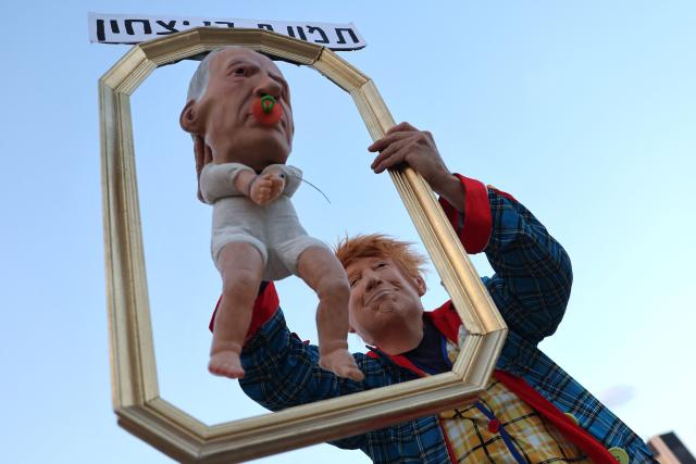 An Israeli left-wing activist in costume with a mask depicting US President Donald Trump holds a baby puppet depicting Israel's Prime Minister Benjamin Netanyahu during a demonstration against the country's ruling government and the ongoing war in the Middle East at the HaBima Square in Tel Aviv on May 16, 2026. (Photo by Jack GUEZ / AFP) / 