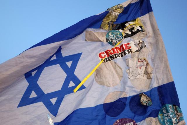 An Israel's flag with pasted stickers is pictured during a demonstration by Israeli left-wing activists against the country's ruling government and the ongoing war in the Middle East at the HaBima Square in Tel Aviv on May 16, 2026. (Photo by Jack GUEZ / AFP)