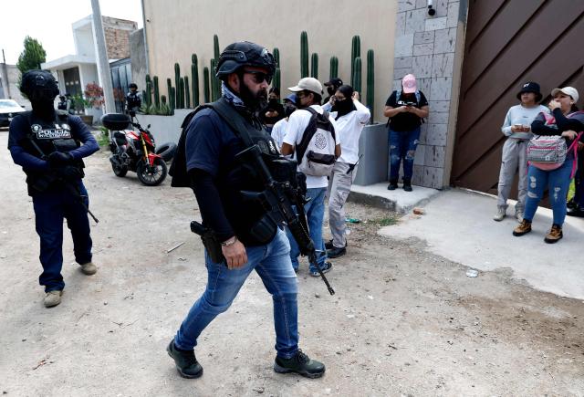Investigative police officers from the Jalisco Attorney General's Office guard the area as Cecilia Flores, activist and founding member of the Madres Buscadoras de Sonora collective, accompanies members of the Madres Buscadoras de Jalisco collective during work at the Las Pintitas mass grave in El Salto, Jalisco state, Mexico, on May 16, 2026. (Photo by ULISES RUIZ / AFP)