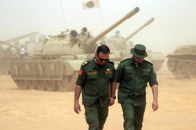 Libyan soldiers walk past tanks as they take part in the "Dara’ al-Karama 2" military exercises, in the Ras al-Alba region in southeastern Libya on May 16, 2026. The military exercises involve extensive participation from various ground, air, and naval units, making them one of the largest exercises the Libyan Army has conducted in recent years, with more than 25,000 military personnel taking part. (Photo by Abdullah DOMA / AFP)