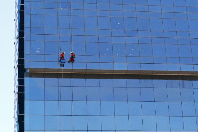 Workers dangle from ropes as they clean the glass panels of a building in Kuwait City on May 17, 2026. (Photo by YASSER AL-ZAYYAT / AFP)