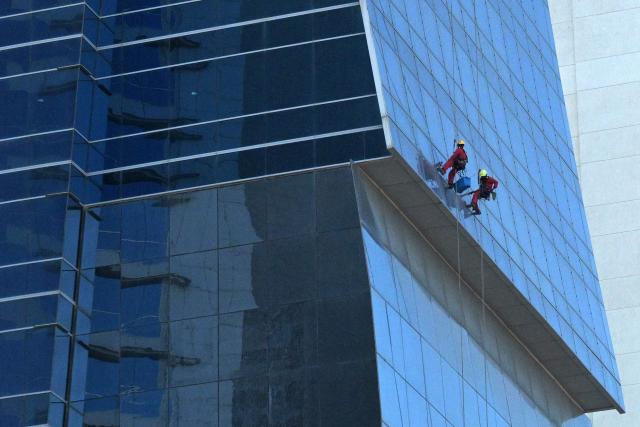 Workers dangle from ropes as they clean the glass panels of a building in Kuwait City on May 17, 2026. (Photo by YASSER AL-ZAYYAT / AFP)