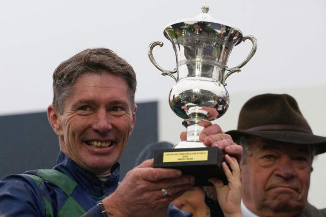French jockey Johnny Charron holds the winner's trophy on the podium next to French horse trainer Guillaume Macaire after winning on "Sel Jem" the 148th edition of the 'Grand Steeple-Chase de Paris' steeplechase horse race at The Auteuil Hippodrome in Paris on May 17, 2026. (Photo by Dimitar DILKOFF / AFP)