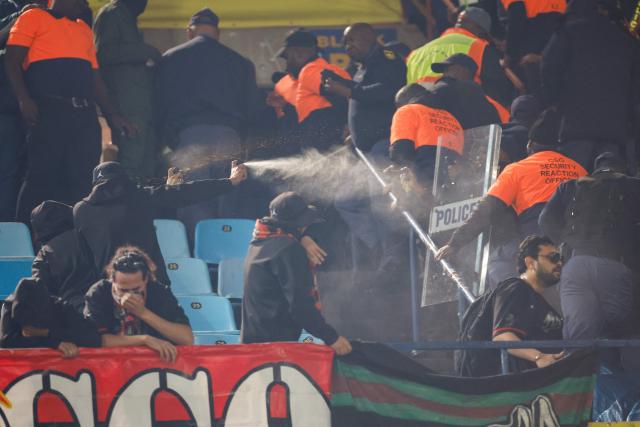 AS FAR supporters spray pepper spray towards security guards and South African Police Service (SAPS) officers as they clash in the stands during the CAF Champions League final first leg football match between Mamelodi Sundowns and AS FAR (Association Sportive des Forces Armees Royales - Royal Army Club) at Loftus Versfeld Stadium in Pretoria on May 17, 2026. (Photo by PHILL MAGAKOE / AFP)