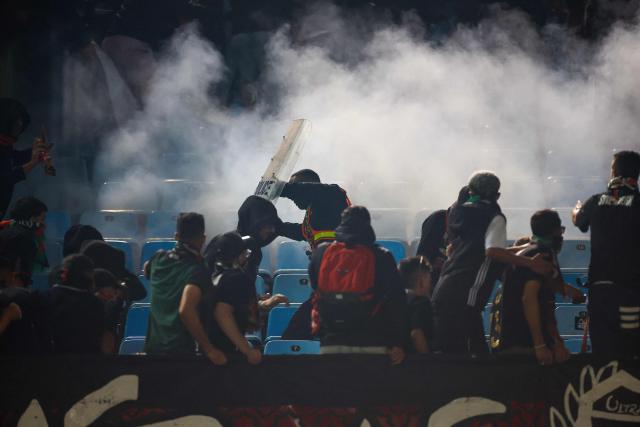 TOPSHOT - AS FAR supporters react after South African Police Service (SAPS) officers fired a smoke grenade as they clash in the stands during the CAF Champions League final first leg football match between Mamelodi Sundowns and AS FAR (Association Sportive des Forces Armees Royales - Royal Army Club) at Loftus Versfeld Stadium in Pretoria on May 17, 2026. (Photo by Phill Magakoe / AFP)