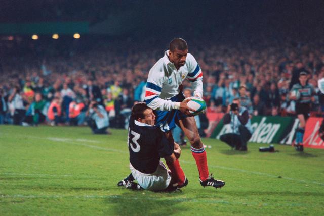(FILES) French right wing Emile N'Tamack (C) is tackled by Scotland's centre Scott Hastings as he scores a try at the last minute of the decisive pool D 1995 World Cup Rugby Union match between France and Scotland at Loftus in Pretoria on June 3, 1995. Scotland great Scott Hastings died at the age of 61 on May 17, 2026, after suffering from cancer, the Scottish Rugby Union has announced. (Photo by Philip LITTLETON / AFP)