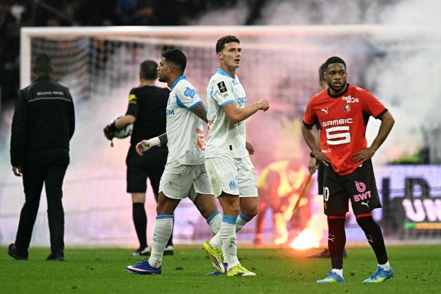 Marseille's French defender #28 Benjamin Pavard and Rennes' French forward #10 Ludovic Blas react as supporters' flares are on the pitch with smoke in the background at the end of the French L1 football match between Olympique de Marseille (OM) and Stade Rennais FC at the Stade Velodrome in Marseille, southern France, on May 17, 2026. (Photo by Gabriel BOUYS / AFP)