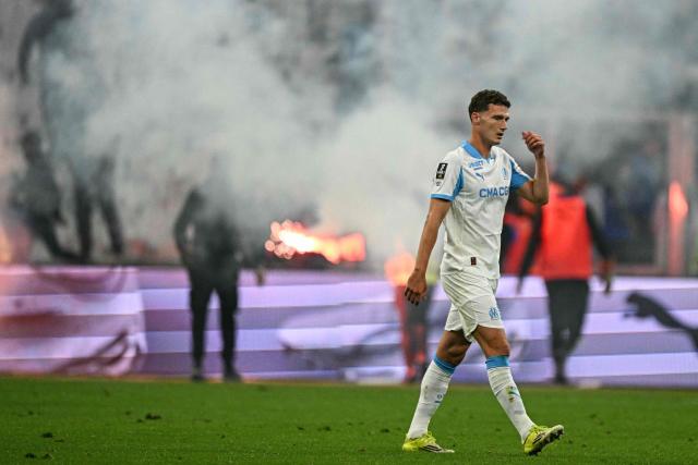 Marseille's French defender #28 Benjamin Pavard reacts as supporters' flares with smoke are seen in the background at the end of the French L1 football match between Olympique de Marseille (OM) and Stade Rennais FC at the Stade Velodrome in Marseille, southern France, on May 17, 2026. (Photo by Gabriel BOUYS / AFP)