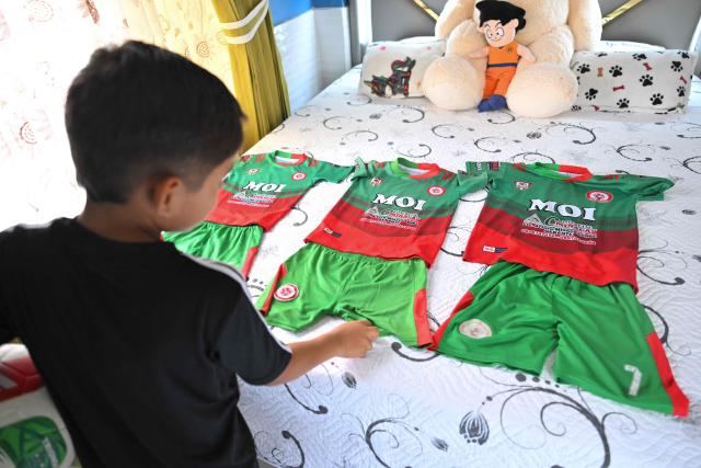 Julian Hidalgo, a fan of Ecuadorian football player Moises Caicedo, shows uniforms from the IG 10 Moises Caicedo football school at his home in Santo Domingo, Ecuador, on May 8, 2026. Amid the tightly packed houses of a working-class Ecuadorian neighborhood, national team football player Moises Caicedo lifted his first trophies. They were made of gold-colored plastic, lent by a neighbor to add excitement to the impromptu game played by a group of children from which one of the world's most highly regarded midfielders emerged. Caicedo, now a Chelsea player, will compete in his second World Cup with Ecuador at just 24 years old. (Photo by Rodrigo BUENDIA / AFP)