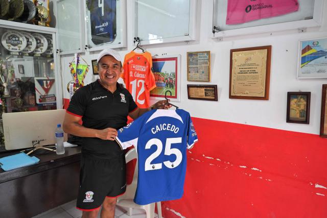 Darwin Castillo, coach of the Jaipadida football school, holds a T-shirt of Ecuadorian football player Moises Caicedo during an interview with AFP in the Cristo Vive neighborhood in Santo Domingo, Ecuador, on May 8, 2026. Amid the tightly packed houses of a working-class Ecuadorian neighborhood, national team football player Moises Caicedo lifted his first trophies. They were made of gold-colored plastic, lent by a neighbor to add excitement to the impromptu game played by a group of children from which one of the world's most highly regarded midfielders emerged. Caicedo, now a Chelsea player, will compete in his second World Cup with Ecuador at just 24 years old. (Photo by Rodrigo BUENDIA / AFP)