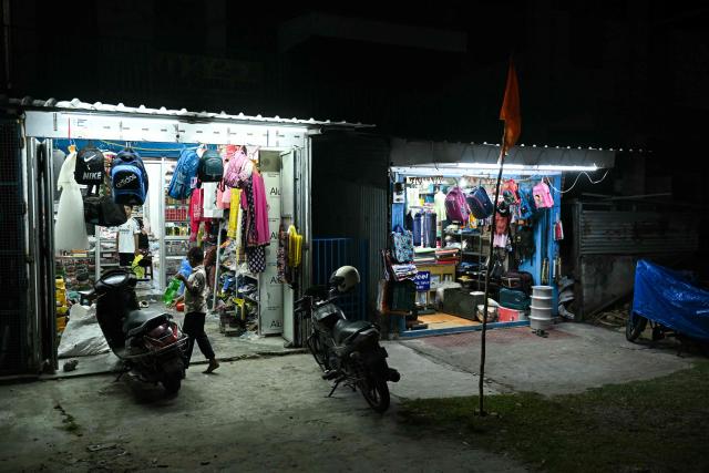 This photograph taken on March 28, 2026 shows a child standing outside a roadside general store at Campbell Bay in Great Nicobar Island. On a remote island in the Andaman Sea, bulldozers are tearing into pristine forests home to one of Earth's most isolated people -- part of India's ambition for a $9 billion megaport, airport and city. Designed to rival China's investments around the Indian Ocean, New Delhi's colossal project will be built on Great Nicobar Island, a site offering a naval presence far closer to Southeast Asia than India's mainland. (Photo by R. Satish BABU / AFP) / TO GO WITH 'India-Nicobar-Politics-Environment-Economy' FOCUS