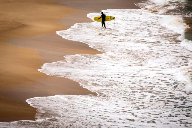 A surfer carries his board as he walks out of the surf at Bondi Beach on a cold autumn day in Sydney on May 18, 2026. (Photo by DAVID GRAY / AFP)