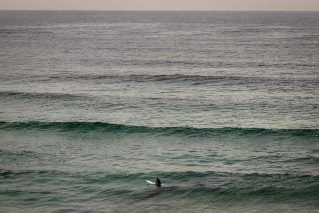 A surfer sits on his board as waves approach at Bondi Beach on a cold autumn day in Sydney on May 18, 2026. (Photo by DAVID GRAY / AFP)