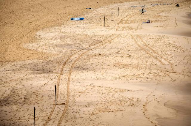 Tracks can be seen in the sand as a surfer carries his board towards the surf at Bondi Beach on a cold autumn day in Sydney on May 18, 2026. (Photo by DAVID GRAY / AFP)