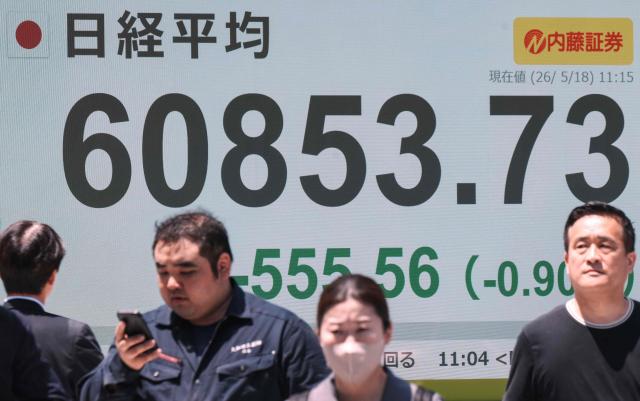 Pedestrians walk past an electronic quotation board displaying the Nikkei Stock Average on the Tokyo Stock Exchange along a street in Tokyo on May 18, 2026. (Photo by Kazuhiro NOGI / AFP)