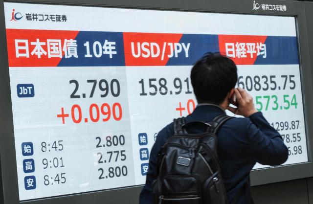 A man walks past an electronic quotation board displaying 10-year Japanese government bonds (L), an index of long-term interest rates on the Tokyo bond market, and the foreign exchange rate of the Japanese yen against the US dollar (C) along a street in Tokyo on May 18, 2026. (Photo by Kazuhiro NOGI / AFP)