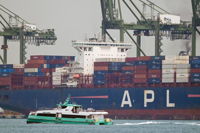 A boat sails past a container vessel docked at Pasir Pajang port terminal in Singapore on May 18, 2026. (Photo by Roslan RAHMAN / AFP)