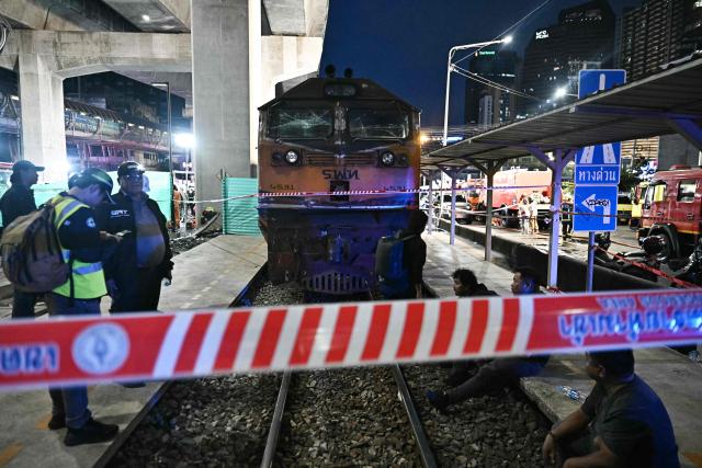 (FILES) Officials stand next to the front of a train that collided with a bus underneath Makkasan Airport Rail station in Bangkok on May 16, 2026. The driver of a train that collided with a bus in Thailand's capital, killing eight people, has tested positive for drugs and was charged with reckless driving, police said on May 18, 2026. (Photo by Lillian SUWANRUMPHA / AFP)