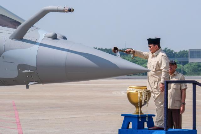 Indonesian President Prabowo Subianto splashes blessed water onto a Rafale jet fighter during a ceremony to hand over six new Rafale jet fighters, six Dassault Falcon 8X aircrafts and two Airbus A400M Atlas transport planes to the Indonesian Air Force at Halim Perdanakusuma Air Force Base in Jakarta on May 18, 2026. (Photo by BAY ISMOYO / AFP)