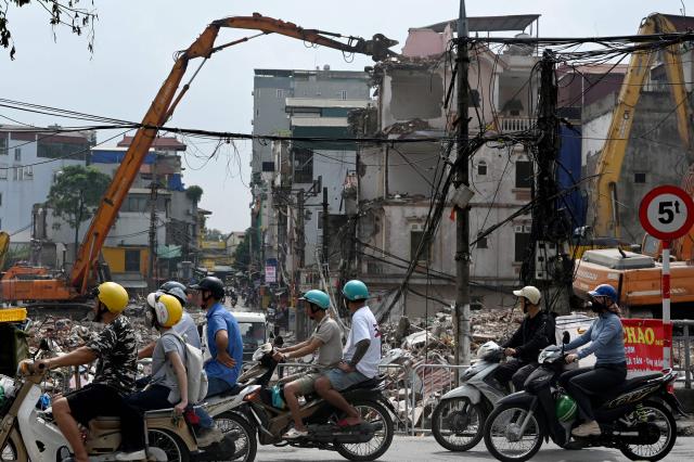 People ride motorcycles past a demolition site of former residential buildings to make way for an expanded road network in Hanoi on May 18, 2026. (Photo by Nhac NGUYEN / AFP)