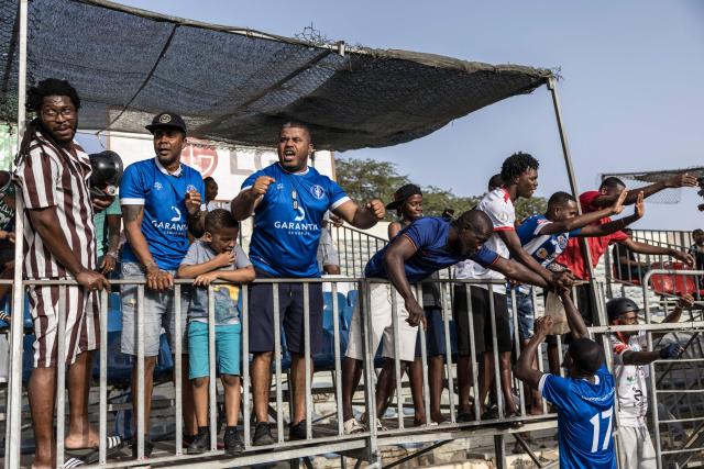 Desportivo da Praia supporters celebrate with players after winning the Praia Cup final football match between Desportivo da Praia and Sporting Clube da Praia at the Estadio da Varzea in Praia, on April 4, 2026. Both teams played the final for a chance to qualify for the Cape Verdean Cup, a knockout tournament that brings together the champions of each island. 
This archipelago of 10 islands is the smallest African nation ever to qualify for a World Cup with a population of just 550,000. 
The national team, known as the Blue Sharks, will compete in Group H against Spain, Saudi Arabia, and Uruguay. 
Their World Cup qualification has inspired many players in the local leagues, who now dream of joining the national team and representing their country. (Photo by PATRICK MEINHARDT / AFP)