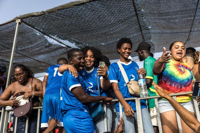 Desportivo da Praia supporters celebrate with players after winning the Praia Cup final football match between Desportivo da Praia and Sporting Clube da Praia at the Estadio da Varzea in Praia, on April 4, 2026. Both teams played the final for a chance to qualify for the Cape Verdean Cup, a knockout tournament that brings together the champions of each island. 
This archipelago of 10 islands is the smallest African nation ever to qualify for a World Cup with a population of just 550,000. 
The national team, known as the Blue Sharks, will compete in Group H against Spain, Saudi Arabia, and Uruguay. 
Their World Cup qualification has inspired many players in the local leagues, who now dream of joining the national team and representing their country. (Photo by PATRICK MEINHARDT / AFP)