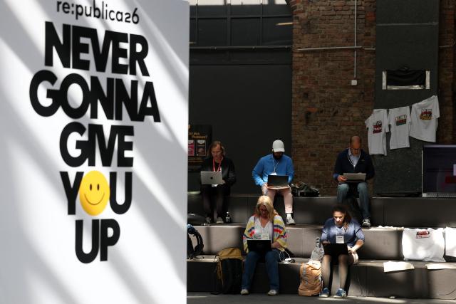 This general overview shows visitors sitting with laptops at the Re:Publica fair ground with a text on a board reading 'Never gonna give you up' at the Re:Publica fair ground during the opening day of the Re:publica digital conference in Berlin, Germany, on May 18, 2026. (Photo by Odd ANDERSEN / AFP)