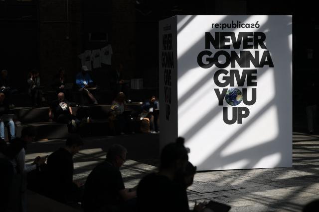 This general overview shows visitors sitting with laptops at the Re:Publica fair ground with a text on a board reading 'Never gonna give you up' at the Re:Publica fair ground during the opening day of the Re:publica digital conference in Berlin, Germany, on May 18, 2026. (Photo by Odd ANDERSEN / AFP)
