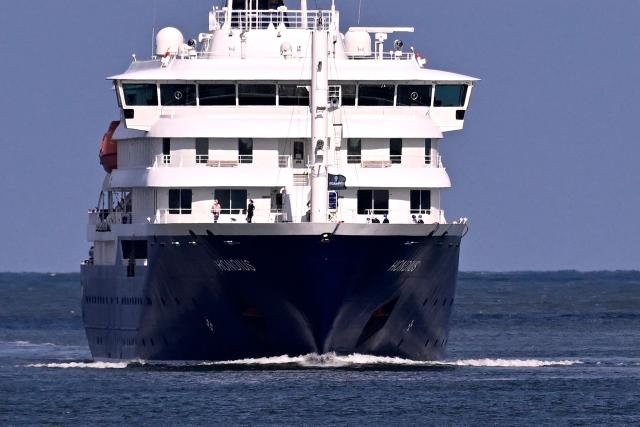 Passengers stand aboard the Dutch Hantavirus-hit cruise ship MV Hondius as it sails off the Netherlands' coast as it approaches the port of Rotterdam on May 18, 2026. Cruise ship MV Hondius is expected to arrive at the port of Rotterdam and the ship's crew members will undergo a medical screening. (Photo by JOHN THYS / AFP)