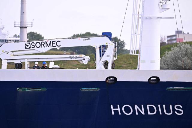 Crew members wearing face masks stand aboard the Dutch Hantavirus-hit cruise ship MV Hondius as it sails off the Netherlands' coast as it approaches the port of Rotterdam on May 18, 2026. Cruise ship MV Hondius is expected to arrive at the port of Rotterdam and the ship's crew members will undergo a medical screening. (Photo by JOHN THYS / AFP)