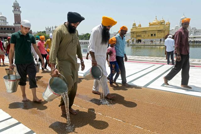 Sikh volunteers pour water on mats laid for devotees on a hot summer day at the Golden Temple in Amritsar on May 18, 2026. (Photo by Narinder NANU / AFP)