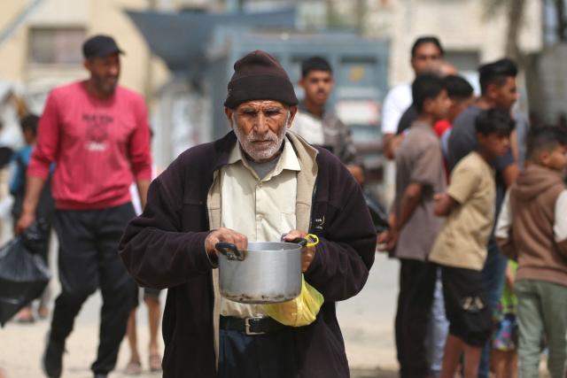 A displaced Palestinian man walks back to his family shelter with a pot of food collected from a charity kitchen, in the Bureij refugee camp, in the central Gaza Strip on May 18, 2026. The war has displaced nearly Gaza's entire population and reduced swathes of the Palestinian territory to rubble despite a ceasefire in October 2025, the enclave remains gripped by daily violence as Israeli strikes continue, with both the military and Hamas accusing one another of violating the truce. Hundreds of thousands of people are still living in tents and conditions remain dire despite a ceasefire that took effect in October last year. (Photo by Eyad Baba / AFP)