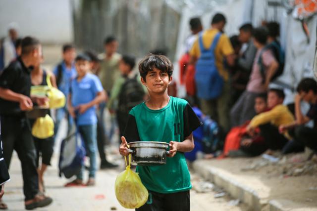 A displaced Palestinian boy carries a pot of food collected from a charity kitchen to his family shelter, in the Bureij refugee camp, in the central Gaza Strip on May 18, 2026. The war has displaced nearly Gaza's entire population and reduced swathes of the Palestinian territory to rubble despite a ceasefire in October 2025, the enclave remains gripped by daily violence as Israeli strikes continue, with both the military and Hamas accusing one another of violating the truce. Hundreds of thousands of people are still living in tents and conditions remain dire despite a ceasefire that took effect in October last year. (Photo by Eyad Baba / AFP)