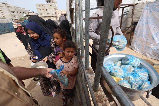 A displaced Palestinian child collects a packet of bread as others wait their turn from a charity kitchen in the Bureij refugee camp, in the central Gaza Strip on May 18, 2026. The war has displaced nearly Gaza's entire population and reduced swathes of the Palestinian territory to rubble despite a ceasefire in October 2025, the enclave remains gripped by daily violence as Israeli strikes continue, with both the military and Hamas accusing one another of violating the truce. Hundreds of thousands of people are still living in tents and conditions remain dire despite a ceasefire that took effect in October last year. (Photo by Eyad Baba / AFP)