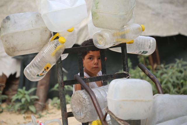 A Palestinian boy stands next to plastic containers on a trolley, as he and others collect portable drinking water for their displaced family living in shelters after homes were destroyed in Israeli bombardment, in the Bureij refugee camp, in the central Gaza Strip on May 18, 2026. The war has displaced nearly Gaza's entire population and reduced swathes of the Palestinian territory to rubble despite a ceasefire in October 2025, the enclave remains gripped by daily violence as Israeli strikes continue, with both the military and Hamas accusing one another of violating the truce. Hundreds of thousands of people are still living in tents and conditions remain dire despite a ceasefire that took effect in October last year. (Photo by Eyad Baba / AFP)