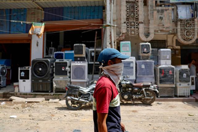 A boy with his face covered with cloth walks past air coolers displayed outside a shop on a hot summer day in Varanasi on May 18, 2026. (Photo by Niharika KULKARNI / AFP)